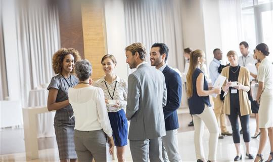 Image shows group of well dressed business men and women stood talking after conference meeting